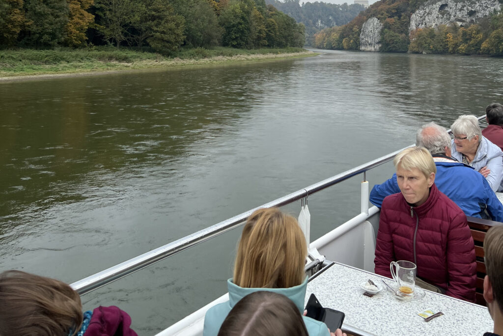 Mitarbeitende sitzen auf dem Außendeck eines Ausflugsschiffs und schauen während der Flussfahrt auf die vorbeiziehende Landschaft.