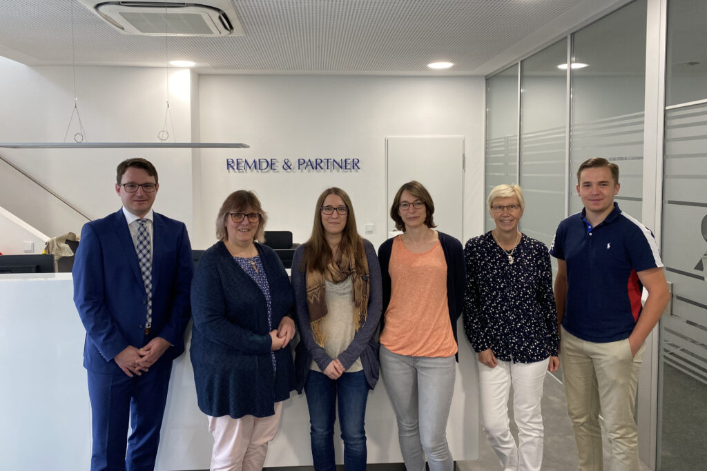Gruppenfoto des Teams von Remde & Partner in den Kanzleiräumen am Empfang mit dem Kanzlei-Schriftzug im Hintergrund.