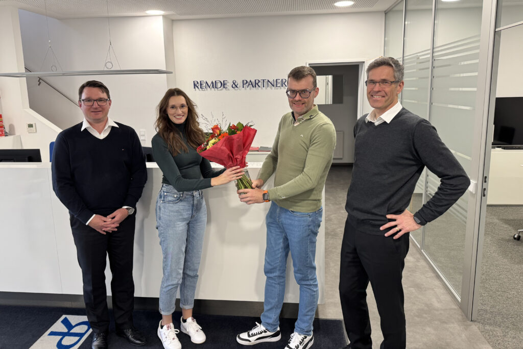 Vier Personen stehen in der Kanzlei von Remde & Partner am Empfang, eine Mitarbeiterin überreicht einem Kollegen einen Blumenstrauß.